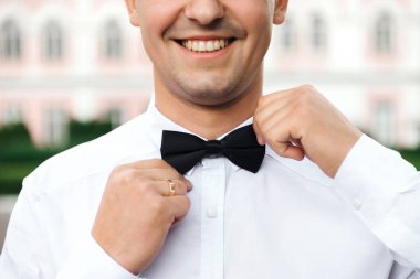 Damat elleriyle bir kelebek tutuyor ve yakından gülümsüyor.