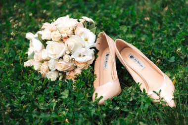 Bir buket beyaz gül ve çimlerin üzerinde gelinin bej rengi ayakkabıları.