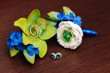 Alyanslar, damatlar yaka çiçekleri ve tahta arka planda gelin küpeleri.