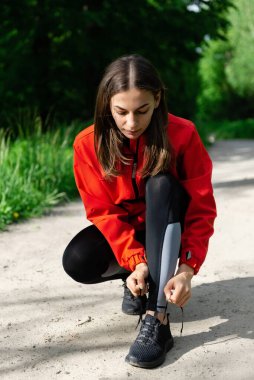 Genç bir kız yaz orman yolunda koşmadan önce ayakkabı bağcıklarını bağlıyor.
