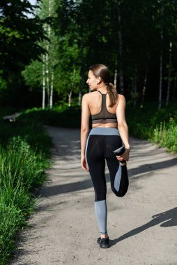 Genç kız ormanda antrenmandan önce ısınıyor. Arkadan görünüm