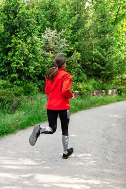 Genç kız orman manzarasında arkadan koşuyor.