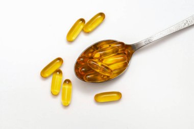Beyaz arka planda kaşık içinde balık yağı kapsülleri
