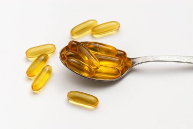 Beyaz arka planda kaşık içinde balık yağı kapsülleri