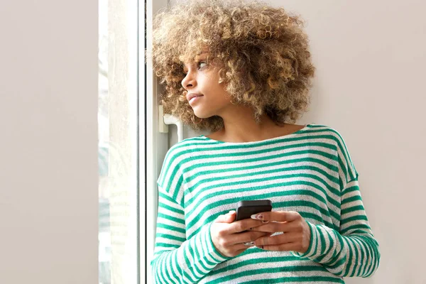 Retrato Una Joven Afroamericana Sosteniendo Teléfono Móvil Mirando Por Ventana —  Fotos de Stock