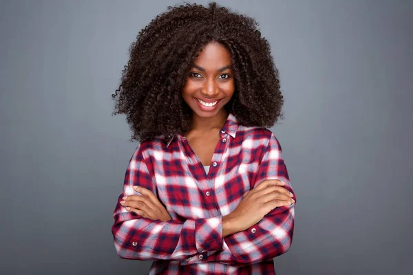 特写微笑年轻非洲妇女在格子衬衣站立与胳膊横渡反对灰色背景的画像 — 图库照片
