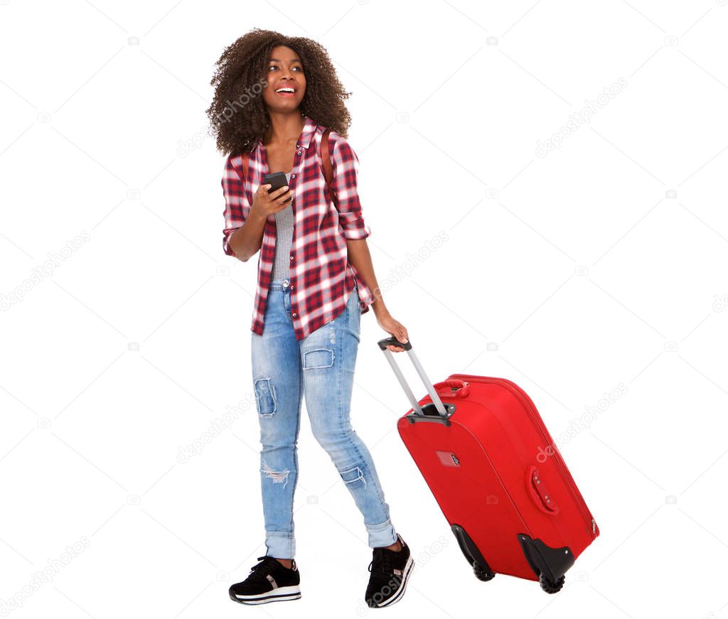 Full body portrait of beautiful young african american woman walking with suitcase and phone on white background