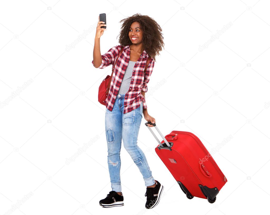 Full body portrait of attractive young african american girl walking with suitcase and taking selfie