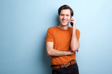 Mavi duvar tarafından cep telefonu ayakta konuşan gülümseyen adam portresi