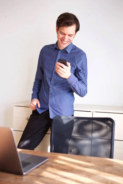 携帯電話を保持しているホーム オフィスに立っている笑みを浮かべて男の肖像 — ストック写真