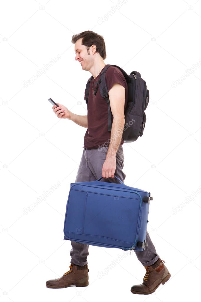 Full length side portrait of traveler walking with suitcase and mobile phone