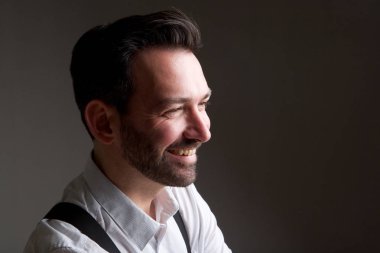 Gri arka planı gülümseyen sakallı yakışıklı adam portresi yan