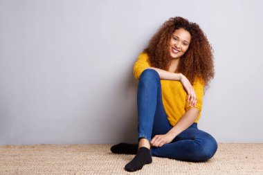 Katta oturan ve gri duvar tarafından gülümseyen Afro-Amerikan Kız portresi