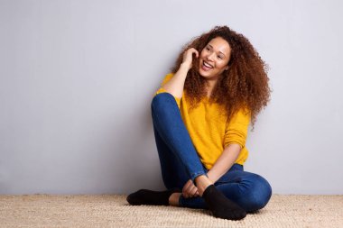 Katta gri duvar dibinde oturan mutlu genç Afro-Amerikan kadın portresi