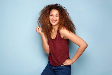 Kıvırcık saçlı mavi arka planı gülümseyen neşeli genç kadın portresi
