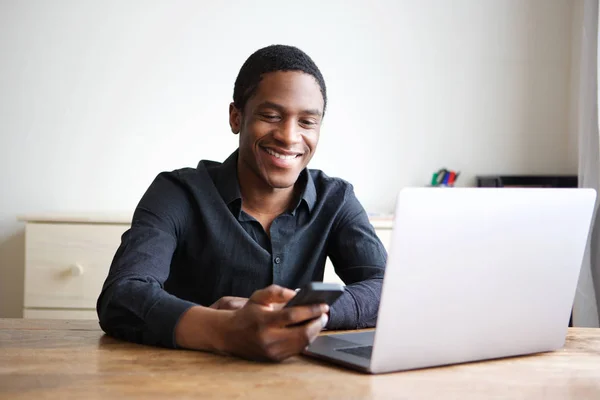 コンピューターの机に座って 携帯電話にテキストを送信する幸せの青年実業家の肖像画 — ストック写真
