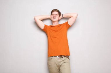 Portrait of happy young man with hands behind head leaning against gray wall clipart