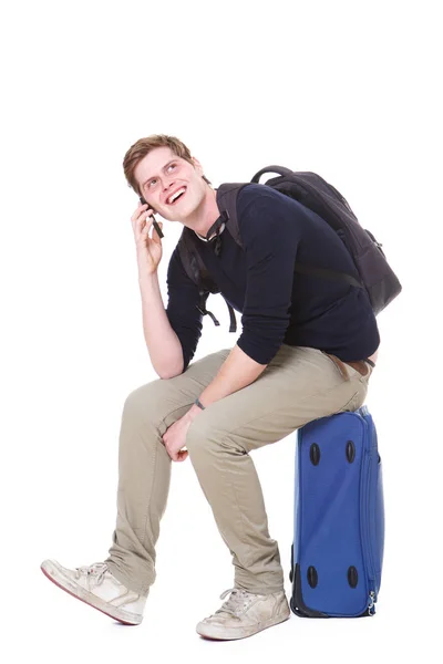スーツケースの上に座って携帯電話で話している幸せの若い男の全身肖像画 — ストック写真
