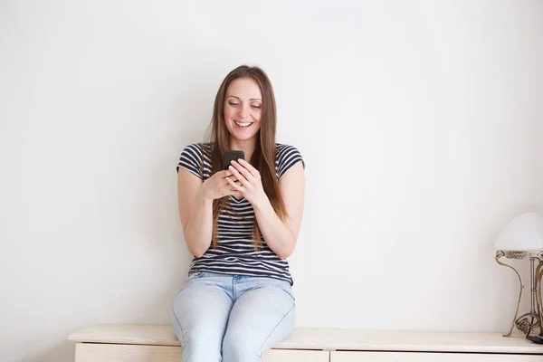 Retrato Joven Feliz Sentada Contra Pared Blanca Mirando Texto Teléfono —  Fotos de Stock