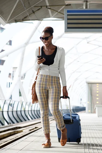 スーツケースと駅で携帯電話と一緒に歩いている楽しい旅女性の全身肖像画 — ストック写真