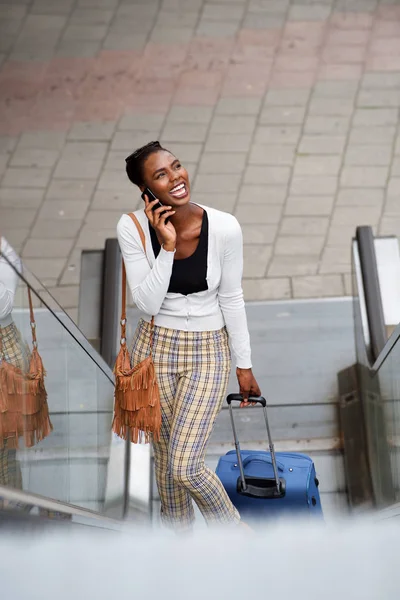 トラベル バッグのエスカレーターの上に立って 携帯電話で話し 幸せのアフリカ系アメリカ人女性の肖像 — ストック写真