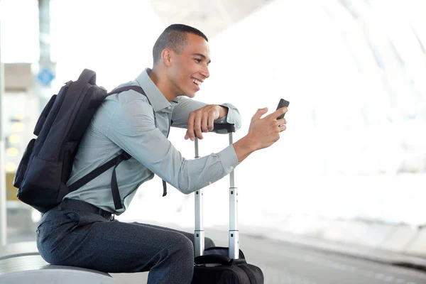 Side portrait of happy traveling businessman looking at mobile phone at station