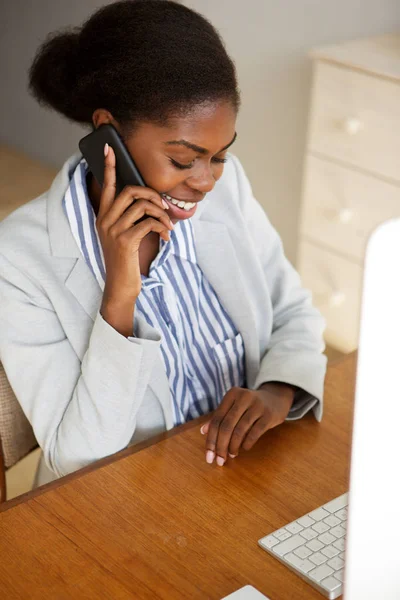 Portrait of smiling young black business woman sitting in office talking on telephone