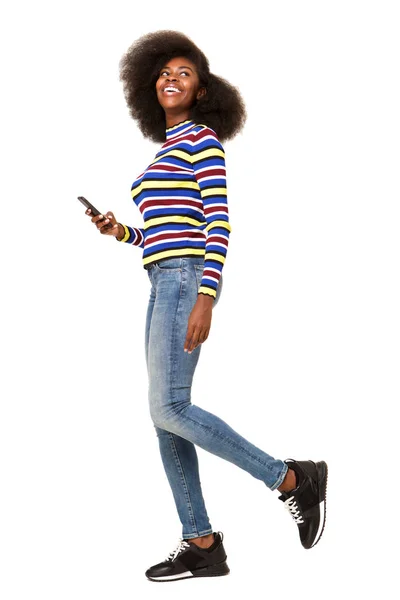 孤立した白い背景に 携帯電話で歩く幸せな若い黒人女性の完全なボディ側の肖像画 — ストック写真