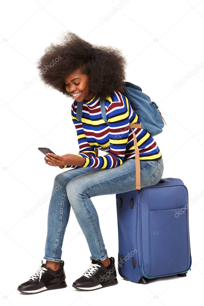 Portrait of young female traveler sitting on suitcase looking at mobile phone 