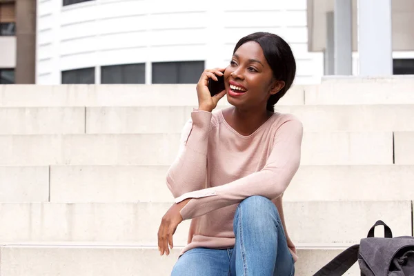 幸せな若い黒人女性外に座っていると携帯電話で話しているの肖像画 — ストック写真