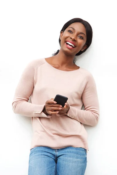 手に携帯電話で白い壁に立って幸せな若い黒人女性の肖像画 — ストック写真