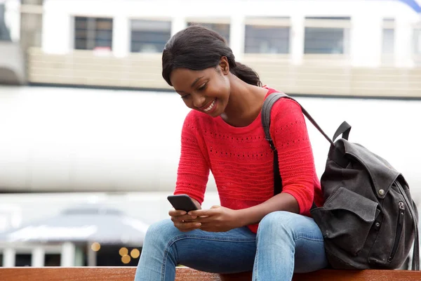 バッグや携帯電話に都市の外に座っている笑顔の若いアフリカ系アメリカ人女性の肖像画 — ストック写真