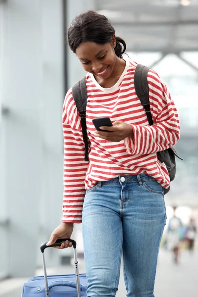 スーツケースと空港で携帯電話と一緒に歩いている若いアフリカ系アメリカ人女性の肖像画 — ストック写真
