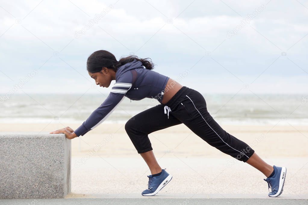Full body side portrait of fit young african american woman stretching muscles at the beach