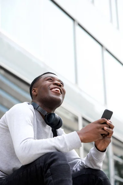 携帯電話で外に座っている陽気な若い黒人男性の肖像画 — ストック写真