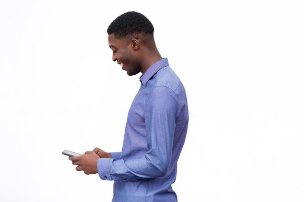 Side portrait of happy young black man standing against isolated white background and looking at mobile phone