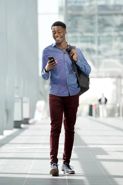 Full body portrait of young black man traveling with bag and mobile phone at station