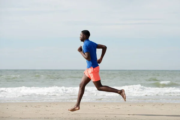 ビーチで実行している健康的なアフリカ系アメリカ人の完全なボディ側の肖像画 — ストック写真