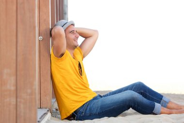 Ellerini başının arkasında ile sahilde kum üzerinde oturan mutlu adam portresi yan