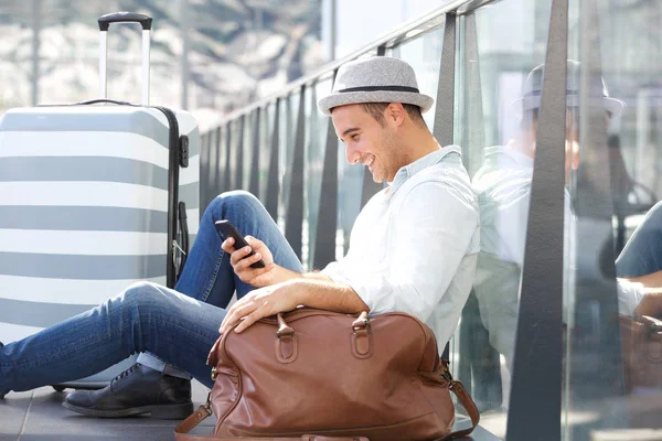 带着手机和包坐在车站地板上的微笑的旅行人的侧画像 — 图库照片
