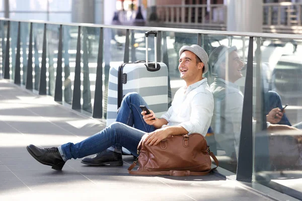 スーツケース バッグや携帯電話が付いている床の上に座って幸せな男の肖像 — ストック写真