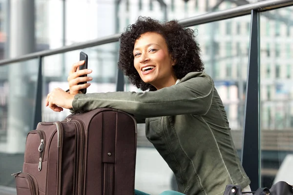 スーツケースと駅で携帯電話を持つ幸せなアフリカ系アメリカ人女性の肖像画 — ストック写真