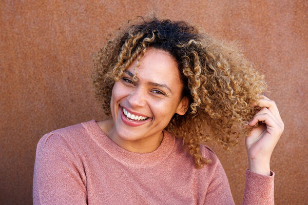 Close up horizontal portrait beautiful african american woman smiling with hand in hair against brown wall