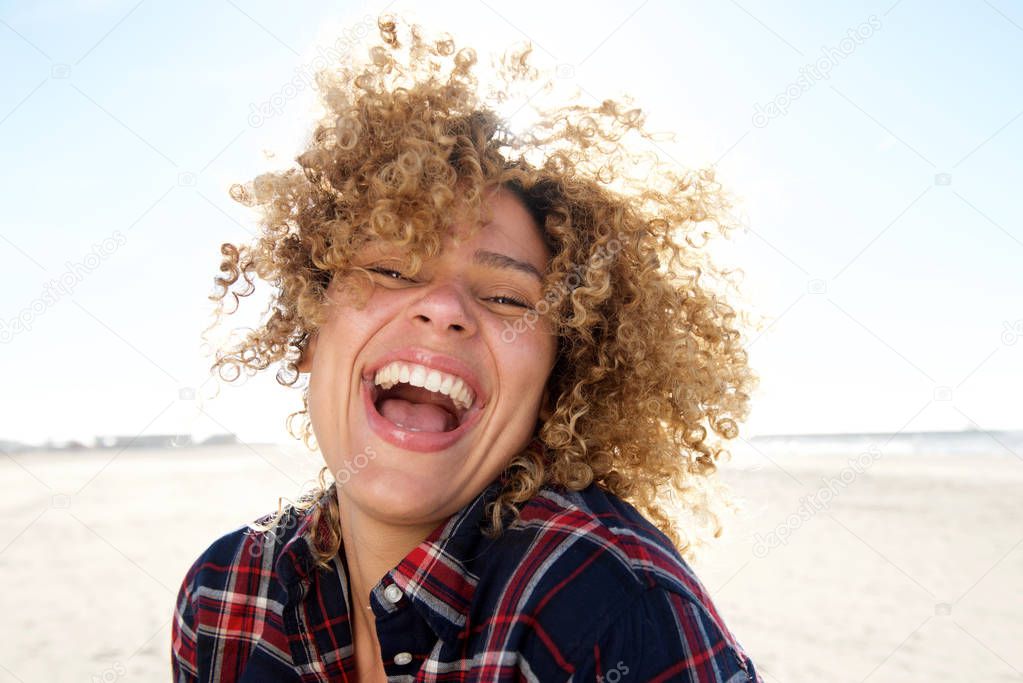 Close up portrait of happy young african american woman laughing at the beach