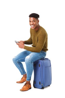 Portrait of happy travel man sitting with cellphone on suitcase against isolated white background