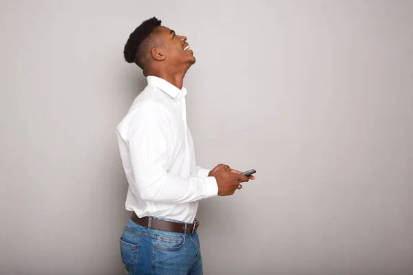 灰色の壁を携帯電話を持って幸せな若い黒人男性の横顔の肖像画 — ストック写真