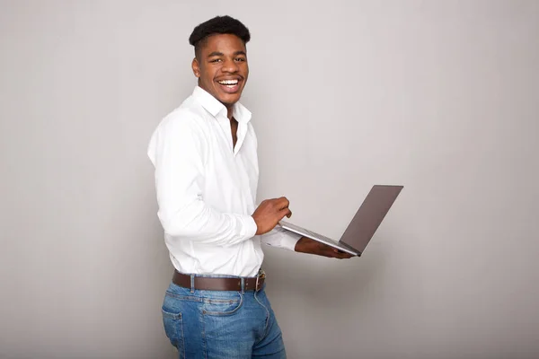 灰色の壁にラップトップを保持している幸せな若い黒人男性の側面の肖像画 — ストック写真