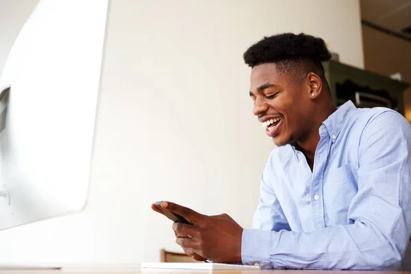 コンピューターで携帯電話で座っている幸せな若いアフリカ系アメリカ人の肖像画 — ストック写真