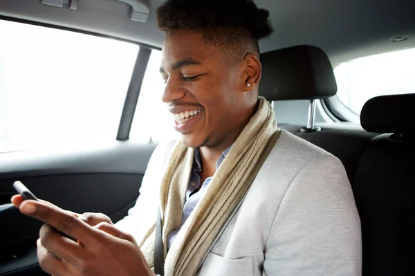 車の後部座席で携帯電話を見て笑顔の若い黒人男性の肖像画 — ストック写真