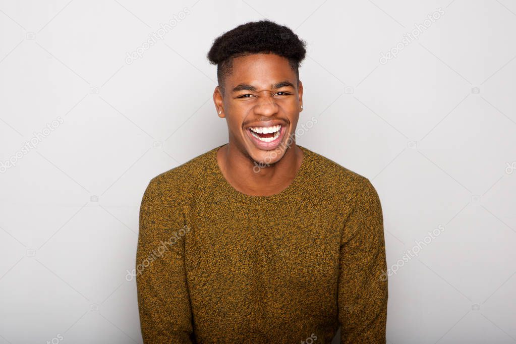 Close up portrait of handsome young african american man laughing by gray wall